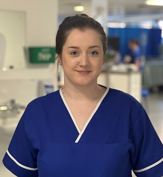 Head and shoulders Photo of Lauren wearing a blue nurse's top with white piping, standing near a ward