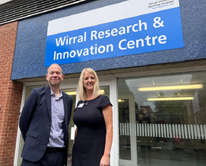 Photo of Dr Nikki Stevenson and Chris Smith standing in front of the entrance to the Wirral Research and Innovation Centre