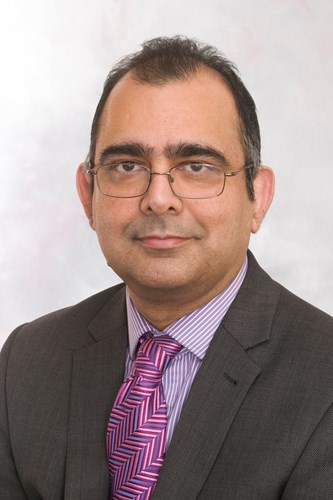 Head and shoulders photo of Monoj  who is wearing glasses, a grey suit and pink tie