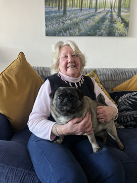 Carole Clayton sitting on a blue sofa with a pug dog on her knee