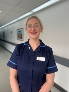 Photo of Annabel Clark who has blond hair and is wearing a navy tunic with light blue piping, glasses.